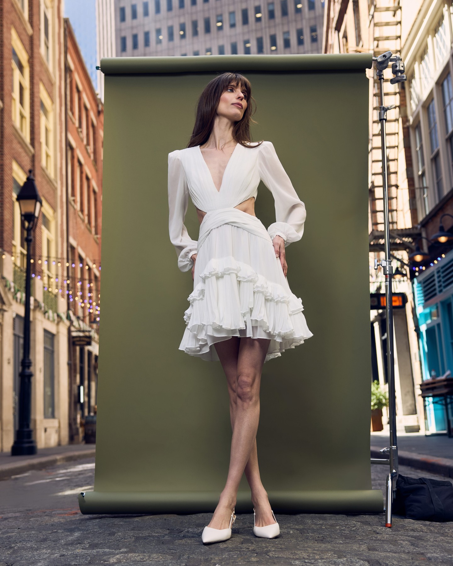 A ruffled white mini dress against an olive backdrop in the street
