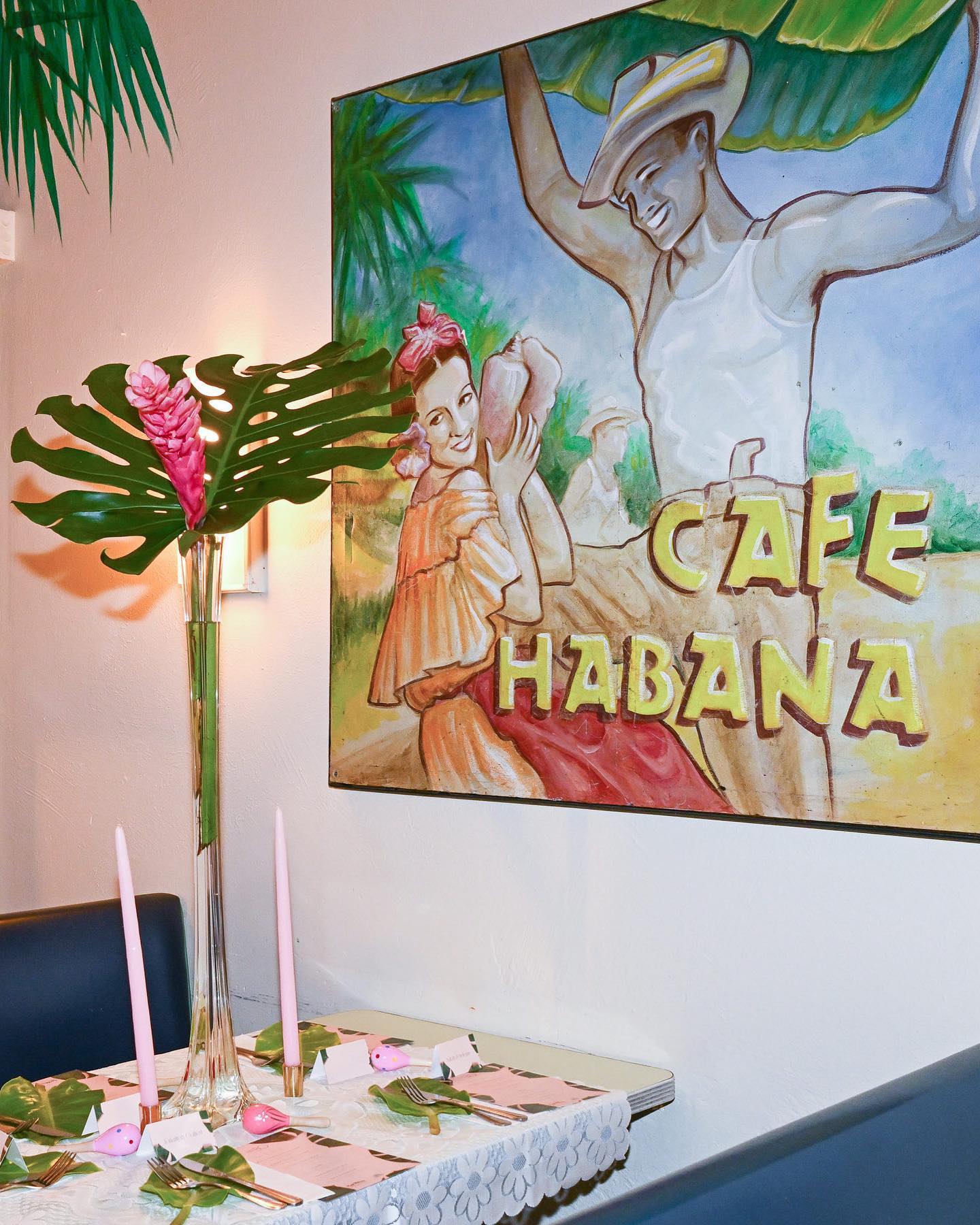 Tablescape of pink candles and monstera under the Café Habana mural